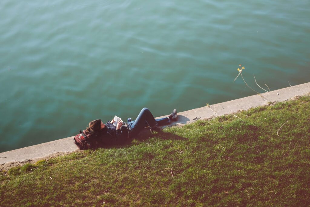 An introvert relaxes by a river reading a book on their own